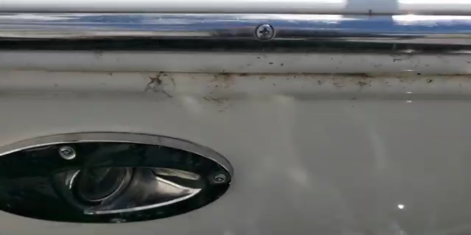 Spider droppings and a web staining the white gelcoat below the rub rail of a boat sitting in a marina.
